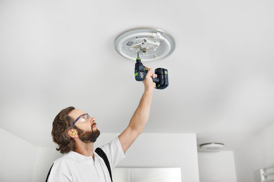 Festool Akku-Bohrschrauber TXS 18 C 3,0-Plus bei Deckeninstallation mit zwei Akkus in Hand eines Handwerkers