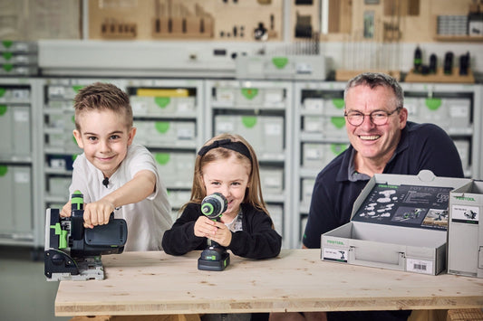 Festool TY-TPC Spielzeug Akku-Bohrschrauber, Erwachsener mit zwei Kindern demonstrieren Bedienung und Zubehör an Werkbank
