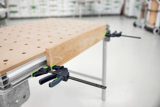 Festool Einhandzwinge FS-EZ 150/2 auf Werkbench mit Holzplatte gespannt, Detailaufnahme des Zwingenkopfs mit Pumphebel.