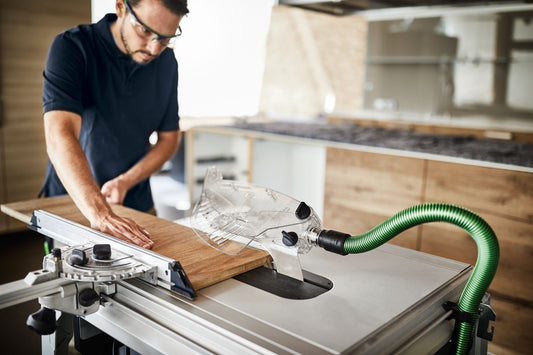 Festool Tischkreissäge TKS 80 EBS mit grünem Absaugschlauch beim Sägen von Holzwerkstück auf Arbeitstisch