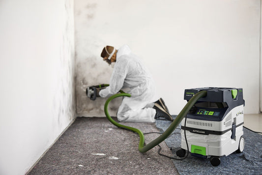 Festool CLEANTEC CTH MIDI I AC Absaugmobil mit grünem Schlauch bei Staubabsaugung an Wand, kompaktes Fahrwerk