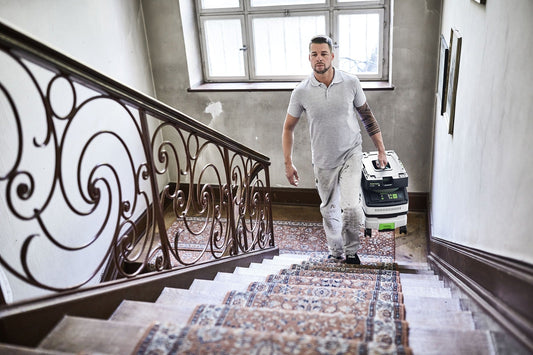 Festool CLEANTEC CTL MINI I Absaugmobil auf Treppe, Handwerkerin trägt kompakten Staubsauger der Klasse L