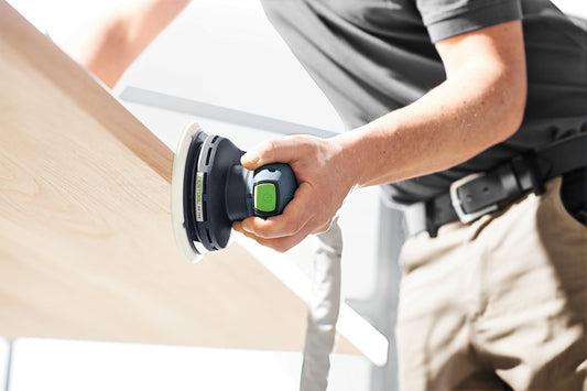 Festool ETS EC 150/3 Exzenterschleifer in Anwendung auf Holzwerkstück mit grünem Schalter in Hand