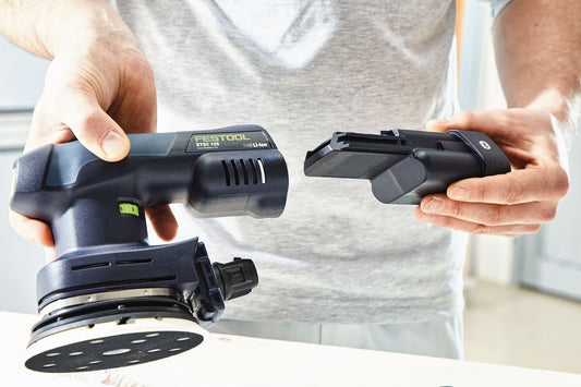 Festool ETSC 125 Akku-Exzenterschleifer mit Schleifteller und Akku, Handgriff und Absaugadapter in Händen.