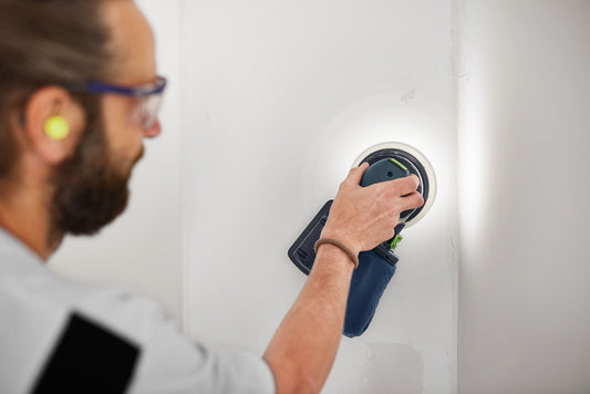 Festool Exzenterschleifer ETSC 2 mit Staubfangbeutel in Anwendung an Wand, Handwerker mit Schutzbrille