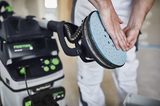 Festool Schleifscheibe Granat mit StickFix-Klettsystem wird auf Schleifteller befestigt, im Hintergrund Elektroschleimaschine